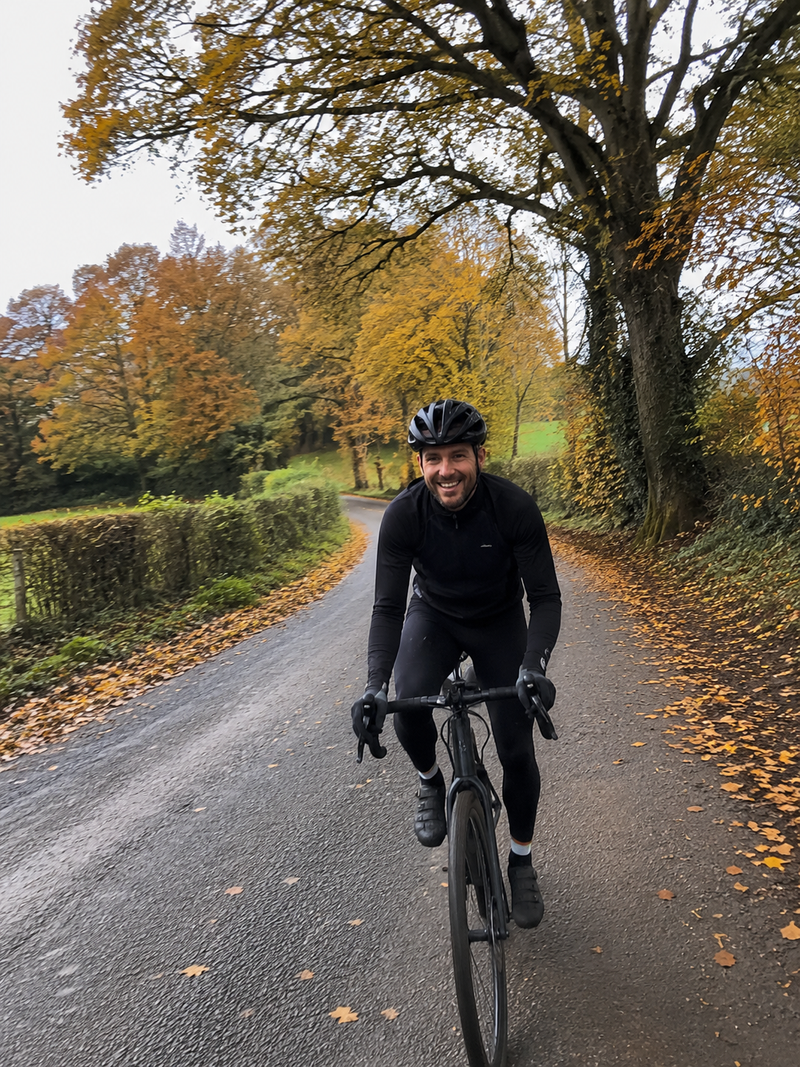 Smiling cyclist in black cycling kit riding a road bike down an autumn country lane — AtlasGears